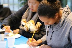 Two participants using their paint brush against a white canvas Two participants using their paint brush against a white canvas